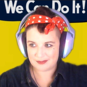 A femme presenting non-binary woman in a blue denim shirt with a red polka dot scarf wrapping up their brown hair a la Rosie the Riveter.